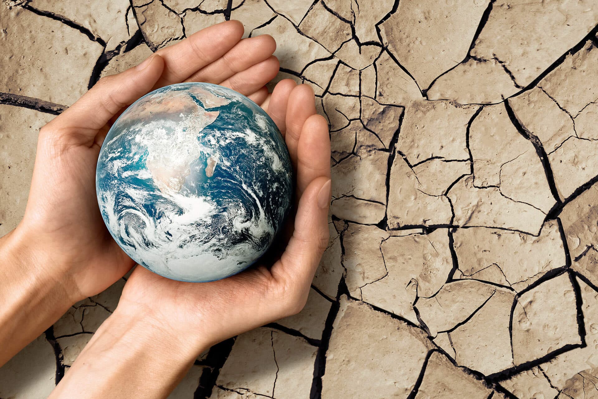 Imagen representativa del cambio climático: dos manos sujetando el planeta tierra sobre un fondo de suelo seco