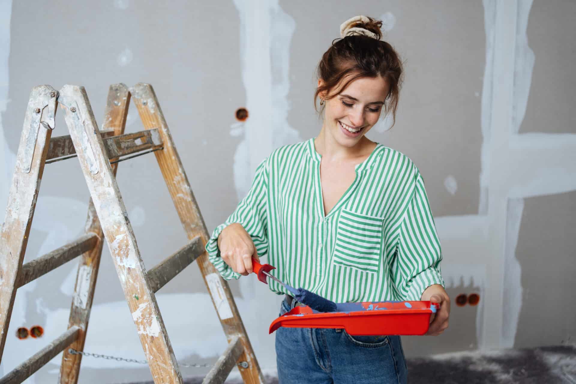 Mujer con escalera de obra en un piso en reforma con un rodillo en la mano preparada para pintar la pared