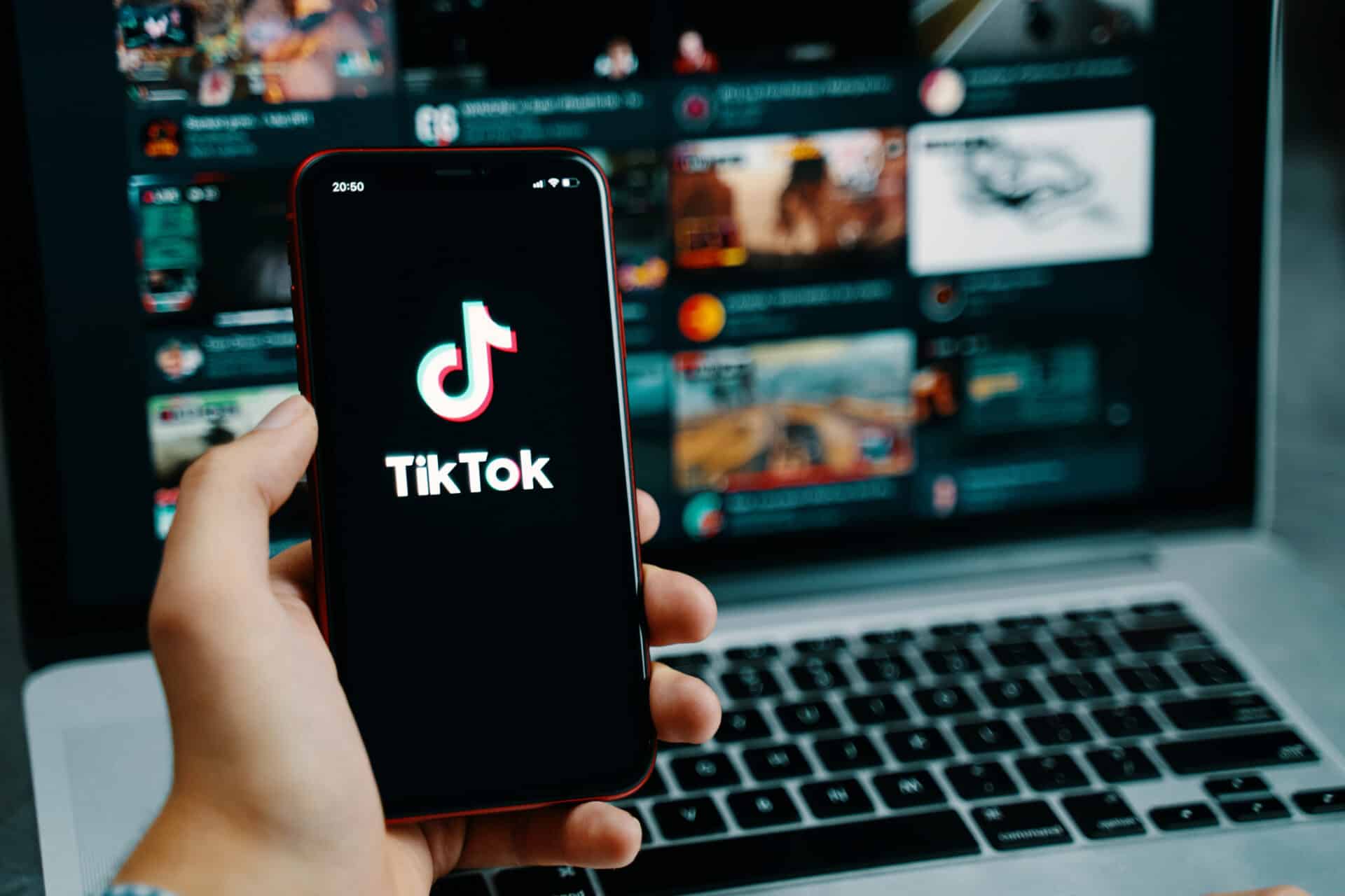 Persona con el móvil en la mano delante de un portátil usando TikTok.